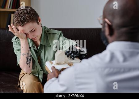 Junge Frau mit Behinderung weint während der Psychotherapiesitzung, während die Psychotherapeutin ihr Gewebe gibt Stockfoto