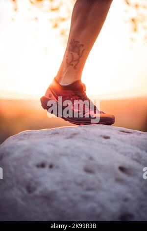 Der Wanderer tritt mit Laufen, Sportschuhen, Sonnenuntergang und Nahaufnahme auf die Steine Stockfoto