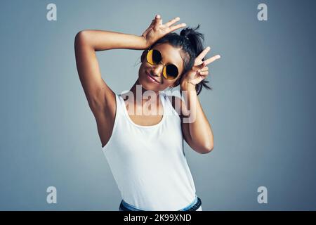 Es fühlt sich funkig und funky an. Studioportrait einer schönen jungen Frau, die mit Hasenohren vor grauem Hintergrund gestikelt wird. Stockfoto