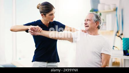 HES lebt sein bestes gesundes Leben. Eine attraktive junge Physiotherapeutin, die mit einem älteren männlichen Patienten arbeitet. Stockfoto