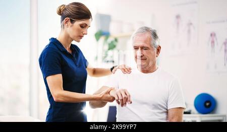Lassen Sie uns etwas an Ihrer Schulter arbeiten. Eine attraktive junge Physiotherapeutin, die mit einem älteren männlichen Patienten zusammenarbeitet. Stockfoto