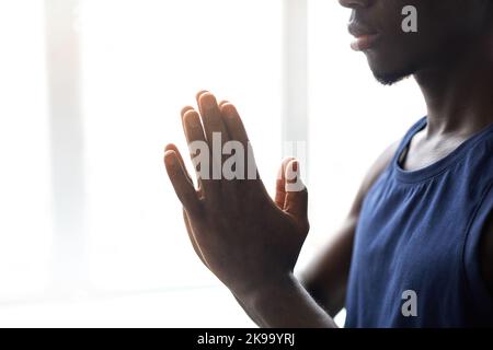 Nahaufnahme eines jungen afrikanischen Mannes, der seine Hände faltete und sich während der Yoga-Praxis auf Meditation konzentrierte Stockfoto