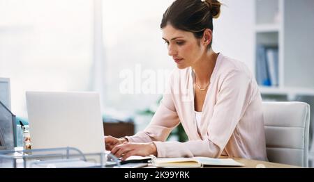 Shes war immer eine harte Arbeiterin. Eine attraktive junge Geschäftsfrau, die in ihrem Büro an einem Laptop arbeitet. Stockfoto