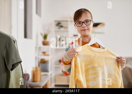 Waist-up-Porträt eines Teenagers mit Down-Syndrom, das Kleidung auswählt und die Kamera anschaut, Raum kopieren Stockfoto