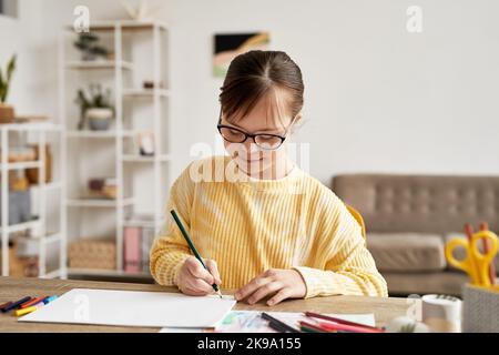 Portrait von Teenager-Mädchen mit Down-Syndrom Zeichnung Bilder am Tisch in gemütlichen Raum und lächelnd, kopieren Raum Stockfoto