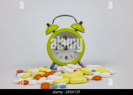 Einnahme von Pillen oder Medikamenten auf Zeit Konzeptfoto. Adhärenz von Medikamenten oder routinemäßiges Hintergrundbild. Pillen und Uhr. Selektiver Fokus auf den Vordergrund. Stockfoto