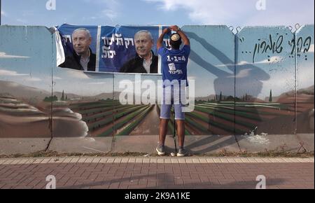 HAWARA, WESTJORDANLAND - 19. OKTOBER: Ein Israeli hängt ein Wahlkampfbanner für die Likud-Partei, auf dem ihr Anführer Benjamin Netanjahu in einer bemalten Stahlbetonbetonbetonwand gegen das Scharfschützenfeuer am 19. Oktober 2022 in der Nähe der palästinensischen Stadt Hawara, südlich von Nablus, Westjordanland, abgebildet ist. Weniger als zwei Wochen vor Israels fünfter Wahl in vier Jahren, inmitten der eskalierenden Gewalt im Westjordanland, prognostiziert die Umfrage eine niedrige israelische arabische Wahlbeteiligung, die Benjamin Netanjahu und der extremen Rechten eine parlamentarische Mehrheit den Weg ebnen kann. Kredit: Eddie Gerald/Alamy Live Nachrichten Stockfoto