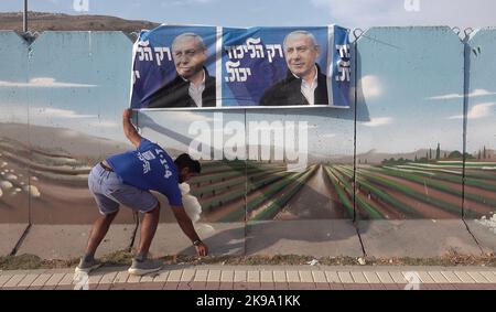 HAWARA, WESTJORDANLAND - 19. OKTOBER: Ein Israeli hängt ein Wahlkampfbanner für die Likud-Partei, auf dem ihr Anführer Benjamin Netanjahu in einer bemalten Stahlbetonbetonbetonwand gegen das Scharfschützenfeuer am 19. Oktober 2022 in der Nähe der palästinensischen Stadt Hawara, südlich von Nablus, Westjordanland, abgebildet ist. Weniger als zwei Wochen vor Israels fünfter Wahl in vier Jahren, inmitten der eskalierenden Gewalt im Westjordanland, prognostiziert die Umfrage eine niedrige israelische arabische Wahlbeteiligung, die Benjamin Netanjahu und der extremen Rechten eine parlamentarische Mehrheit den Weg ebnen kann. Kredit: Eddie Gerald/Alamy Live Nachrichten Stockfoto