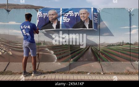 HAWARA, WESTJORDANLAND - 19. OKTOBER: Ein Israeli hängt ein Wahlkampfbanner für die Likud-Partei, auf dem ihr Anführer Benjamin Netanjahu in einer bemalten Stahlbetonbetonbetonwand gegen das Scharfschützenfeuer am 19. Oktober 2022 in der Nähe der palästinensischen Stadt Hawara, südlich von Nablus, Westjordanland, abgebildet ist. Weniger als zwei Wochen vor Israels fünfter Wahl in vier Jahren, inmitten der eskalierenden Gewalt im Westjordanland, prognostiziert die Umfrage eine niedrige israelische arabische Wahlbeteiligung, die Benjamin Netanjahu und der extremen Rechten eine parlamentarische Mehrheit den Weg ebnen kann. Kredit: Eddie Gerald/Alamy Live Nachrichten Stockfoto