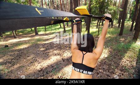 Athletisch, Frau, Ausbilder, führt, macht Übungen . Im Kiefernwald, im Sommer, bei Sonnenstrahlen. Rückansicht. Hochwertige Fotos. Stockfoto