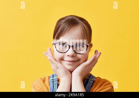 Nahaufnahme Porträt von niedlichen Mädchen mit Down-Syndrom Blick auf die Kamera vor gelbem Hintergrund im Studio Stockfoto