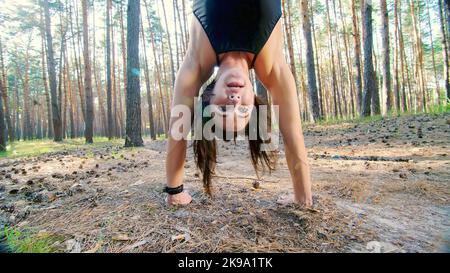 Athletische Frau, Trainerin, Ausbilderin, führt durch, macht Übungen mit. Im Kiefernwald, im Sommer, in den Sonnenstrahlen. Ansicht von unten, Liegestütze.. Hochwertige Fotos Stockfoto