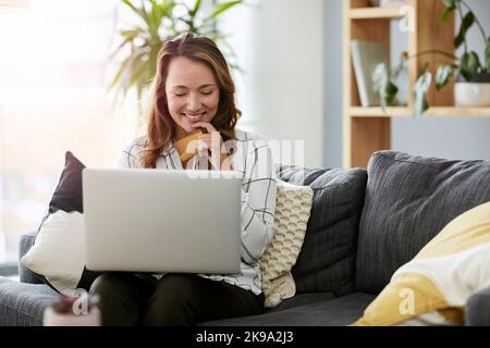 Online-Shopping hat seine Vorteile. Eine attraktive Geschäftsfrau macht Online-Shopping auf ihrem Laptop, während sie sich zu Hause auf ihrem Sofa entspannt. Stockfoto