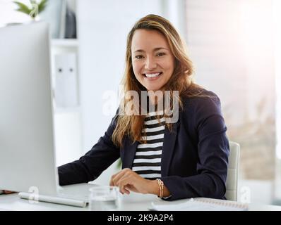 Geschäftsabwicklung auf die beste Art und Weise, wie sie weiß. Porträt einer fröhlichen Geschäftsfrau, die in ihrem Büro am Computer arbeitet. Stockfoto