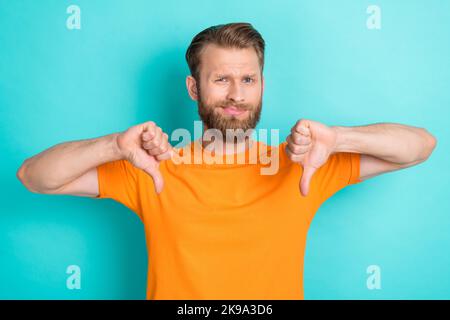 Porträt von traurig unglücklich verärgert Kerl mit blondem Bart tragen orange T-Shirt zeigt Daumen nach unten Abneigung isoliert auf blauem Hintergrund Stockfoto