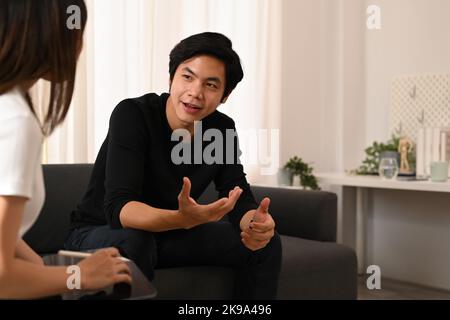 Ein hübscher junger Mann sitzt auf der Couch und hat eine Konsultation mit einem Psychologen. Psychotherapie und psychisches Gesundheitskonzept Stockfoto