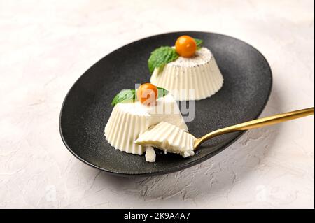 Löffel und Stück hausgemachte Panna Cotta mit natürlicher Vanilleschote, Physalis oder Winterkirsche und Minze, selektiver Fokus Stockfoto