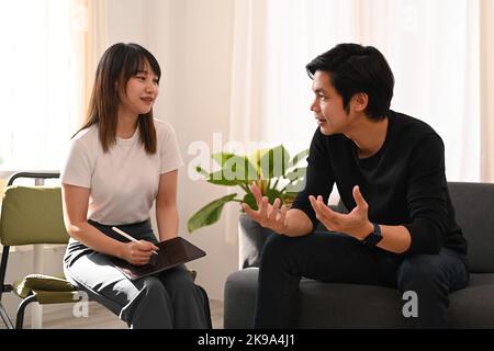 Lächelnde weibliche Psychologin, die Ratschläge gibt und mit Patienten in der psychiatrischen Klinik spricht. Psychotherapiekonzept Stockfoto