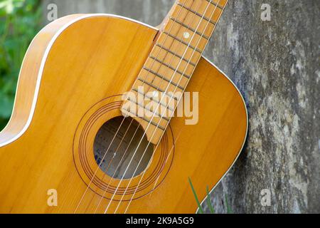 Braune Holzgitarre liegt auf einer Steinstraße in der Straße im Frühlingsgras Stockfoto