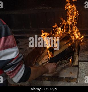 Detail des Armes eines Mannes, der Holzstäbchen anfängt und bewegt, um ein Grillfeuer zu halten Stockfoto