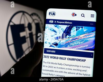 Person, die Mobiltelefon mit der Webseite der Internationalen Automobilföderation (FIA) auf dem Bildschirm vor dem Logo hält. Konzentrieren Sie sich auf die Mitte des Telefondisplays. Stockfoto