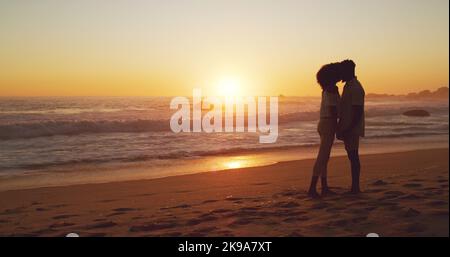 Werde für immer bei dir sein. Ganzkörperaufnahme eines liebevollen jungen Paares, das bei Sonnenuntergang am Strand steht. Stockfoto