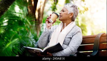 Sie liest immer gerne ihre Bücher im Park. Eine ältere Frau trinkt Kaffee, während sie im Park ein Buch liest. Stockfoto