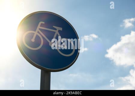 Rundes Straßenschild mit weißem Fahrrad auf blauem Hintergrund, was für Radfahrer einen obligatorischen Radweg vor blauem Himmel bedeutet. Blaues rundes Schild am Fahrradweg-Pol. Radweg Stockfoto