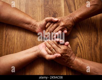 Waren in diesem zusammen. Ein nicht erkennbares Seniorenpaar, das die Hände zu Hause über einem Holztisch zusammenhält, hat eine Aufnahme in einem hohen Winkel gemacht. Stockfoto