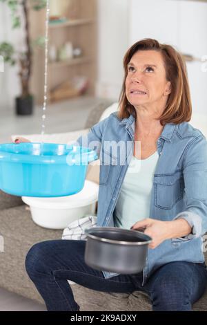 Schockierte Frau, die Wasser aus der Decke sammelte Stockfoto