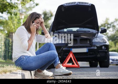 Frau am Telefon neben ihrem kaputten Auto Stockfoto