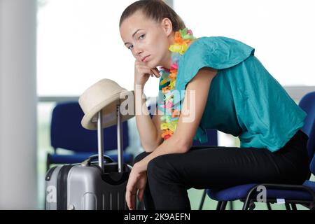 Gelangweilte Frau mit Koffer auf dem Flughafen Stockfoto