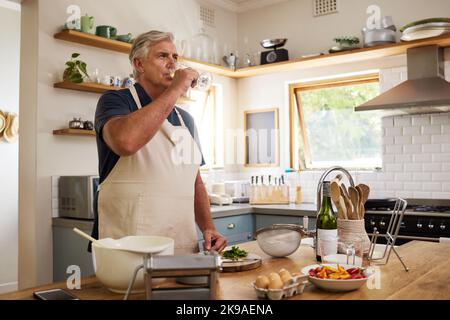 Älterer Mann, trinken Sie Wein in der Küche und entspannen Sie sich nach dem Kochen Essen für eine gesunde Mahlzeit zum Mittagessen zu Hause, glücklich und genießen Sie den Ruhestand. Ältere Menschen, Rentner Stockfoto