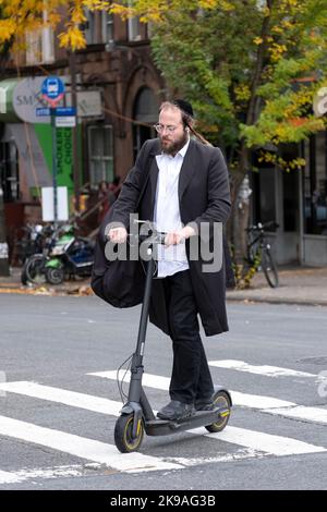 Ein orthodoxer jüdischer Mann überquert die Lee Avenue auf seinem Elektroroller. In Brooklyn, New York, Herbst 2022. Stockfoto