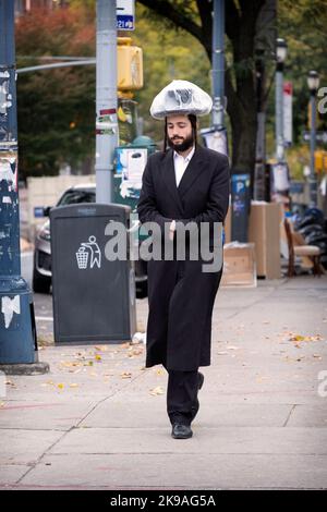 Ein orthodoxer jüdischer Mann, der während eines Nieselzugs auf der Lee Avenue spazierengeht und einen Schutzhelm mit Plastikbeutel trägt. In Brooklyn, NYC, USA. Stockfoto