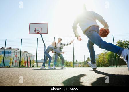 Eine Gruppe von Teenagern, Studenten spielen Straßenkbasketball auf dem Basketballplatz im Freien. Sport, Freizeitaktivitäten, Hobbys, Team, Freundschaft Stockfoto