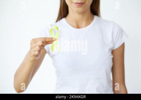 Nahaufnahme einer Frau im weißen T-Shirt, die ein gelbes Bewusstseinsband in ihren Händen hält und zeigt Stockfoto