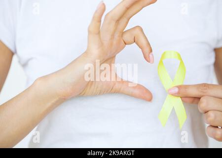 Nahaufnahme einer Frau im weißen T-Shirt, die ein gelbes Bewusstseinsband in ihren Händen hält und zeigt Stockfoto