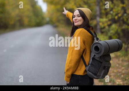 Die junge Frau zeigt mit dem Finger, dass sie vorbeifahrende Autos erwischen muss Stockfoto