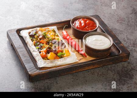Türkischer Kebab mit Kartoffeln, grünen Erbsen, Zwiebeln und Karotten, in Papier eingewickelt und in der Nähe auf einem Holztablett auf dem Tisch gebacken. Horizontal Stockfoto