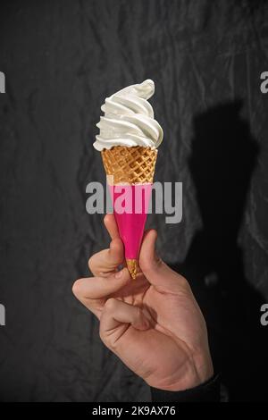 Die Hand hält den Softserve-Eiskonus mit schwarzem Untergrund. Stockfoto