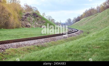 Die selektive FOCUS-Eisenbahnstrecke dreht sich zwischen den Hügeln. Leeres Rundung und Wenden von Einzelbahnen. Perspektivansicht mit flachem Fokus von Stockfoto