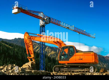 Bagger und Kran auf Baustelle in Wald und Natur. Berge im Hintergrund. Stockfoto