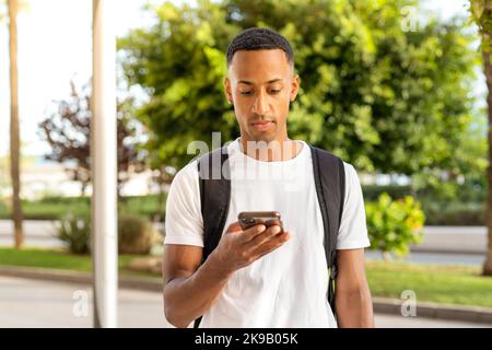 Seitenansicht eines jungen afroamerikanischen Mannes, der glücklich lächelt und das Smartphone auf der Straße der Stadt benutzt. Stockfoto