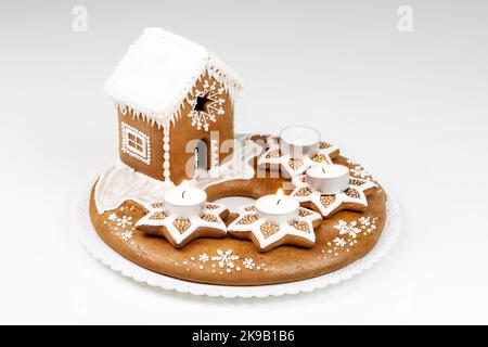 Isolierter Adventskandelhalter mit drei brennenden Kerzen und weihnachtlich hausgemachtem Lebkuchenhaus auf weißem Hintergrund. Stockfoto