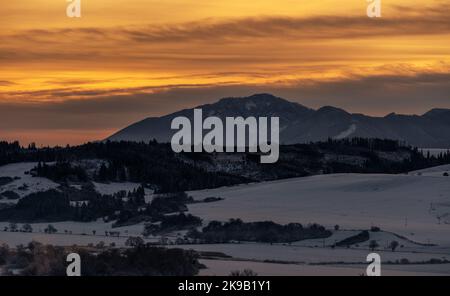Verschneite Winterberglandschaft und farbenfroher Himmel bei Sonnenaufgang über dem Hügel Poludnica in der Niederen Tatra in der Slowakei. Stockfoto