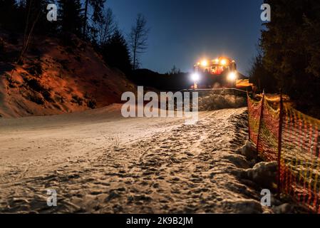 Schneekatzen-Rackmaschine, die im Skigebiet Schnee macht. Schneeräumung bei Nacht. Stockfoto