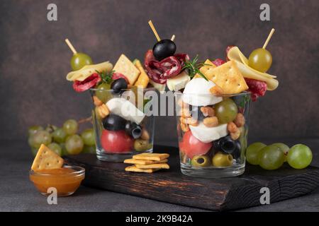 Jarcuterie in zwei Glas umfasst verschiedene Arten von Wurst, Gurken, Käse, Nüsse, Gemüse und Obst. Moderne Version des festlichen Imbisses auf hölzernen bo Stockfoto