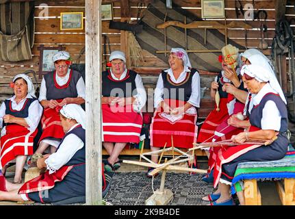 BRASHLYAN, BULGARIEN - 16. JULI 2013: Bulgarische ältere Frauen in Trachten stricken vor dem Haus Stockfoto