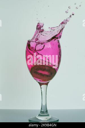 Obst spritzt in Wein, Spirituosen, Cocktailglas, schöne frostigen Rahmen von lebendigen rosa flüssigen Wassertröpfchen in der Luft für Bars, Party, Pubs verstreut.